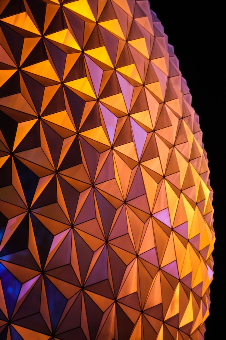 Disney World Epcot's Spaceship Earth glows with orange and yellow reflections at night NotSoSAHM