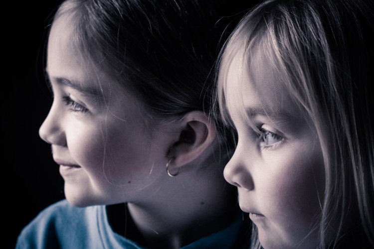 two sisters look out a window with light softly on their faces NotSoSAHM