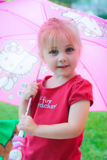 Girl looks out from under a pink umbrella Not So SAHM