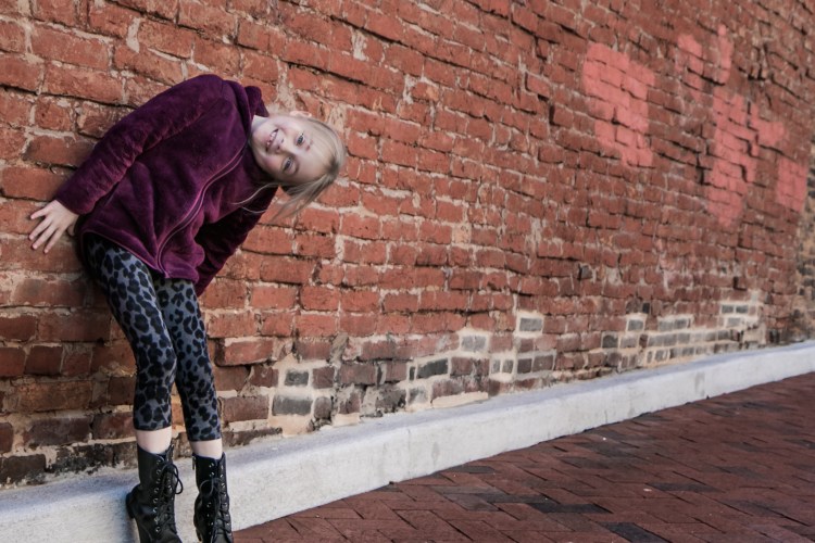 Girl stands in a silly pose in front of brick wall. Not So SAHM