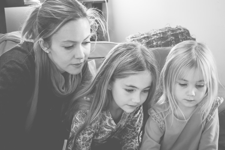 Mom sits with her two daughters, all looking at a computer screen. Not So SAHM